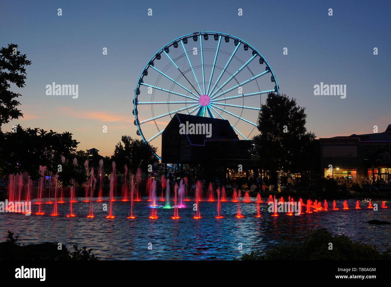 Ferris wheel and water fountain with colored lights at dusk Stock Photo