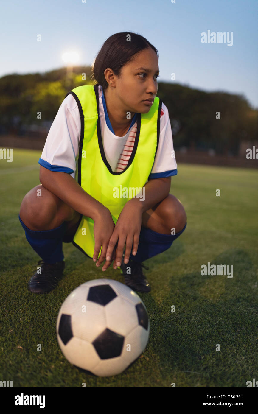 Thoughtful soccer player crouching with football at sports field Stock Photo