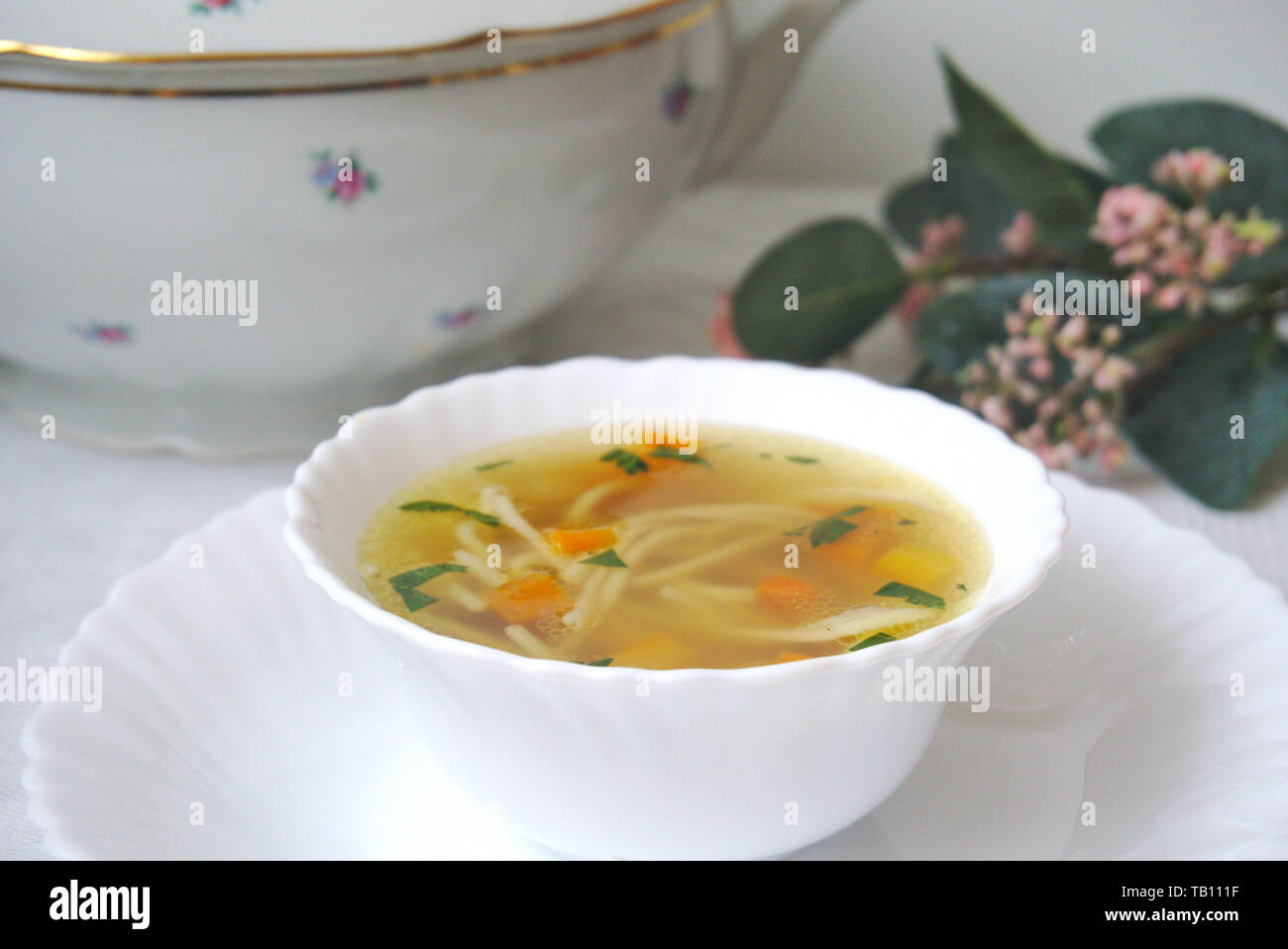 Traditional czech beef broth soup with noodles and vegetables in a white bowl, vintage tableware around Stock Photo