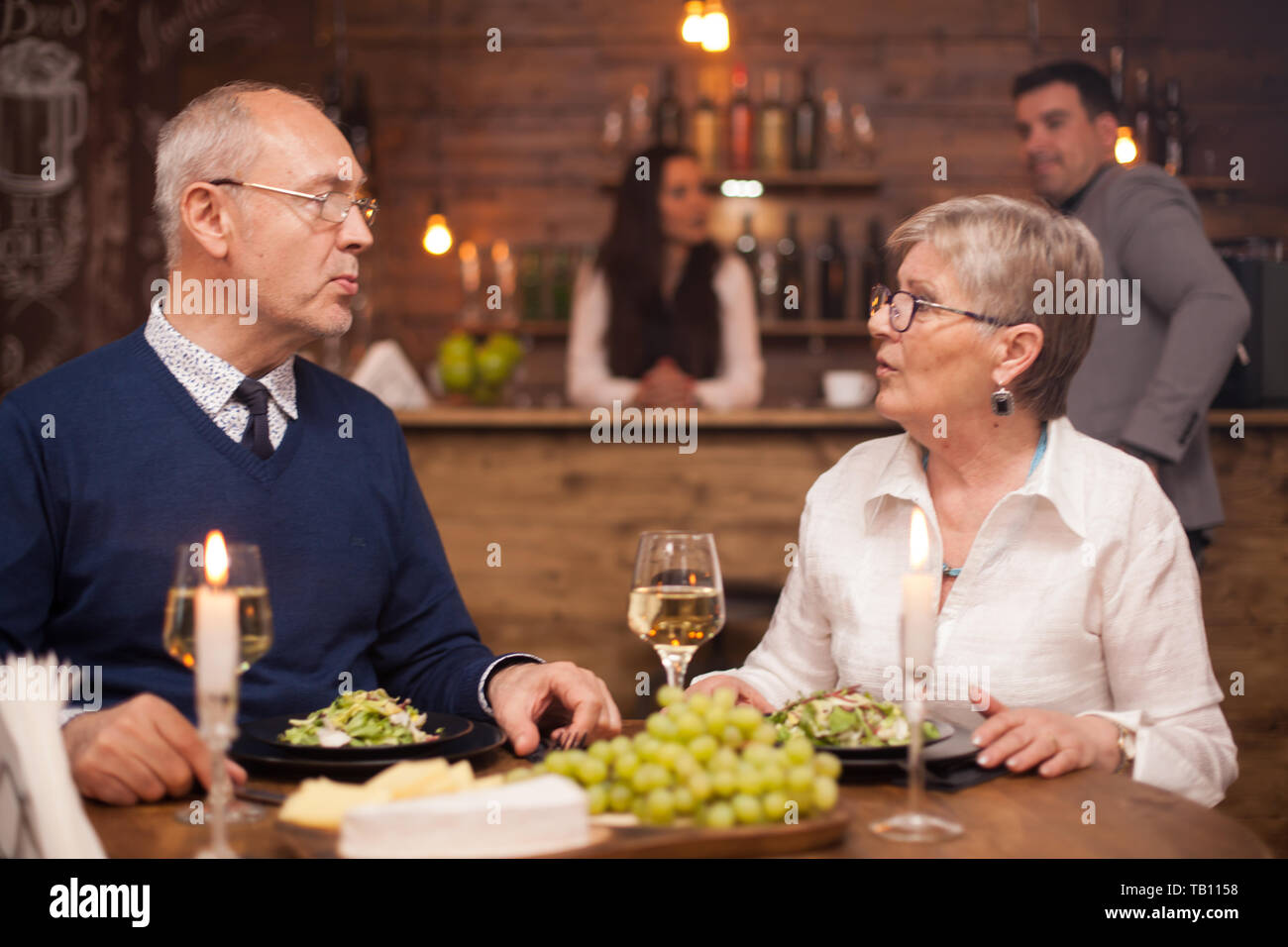 Older sister telling her little brother what she's been up to lately while having dinner in a cozy restaurant. Gresh grapes. Clients blurred in the background. Stock Photo