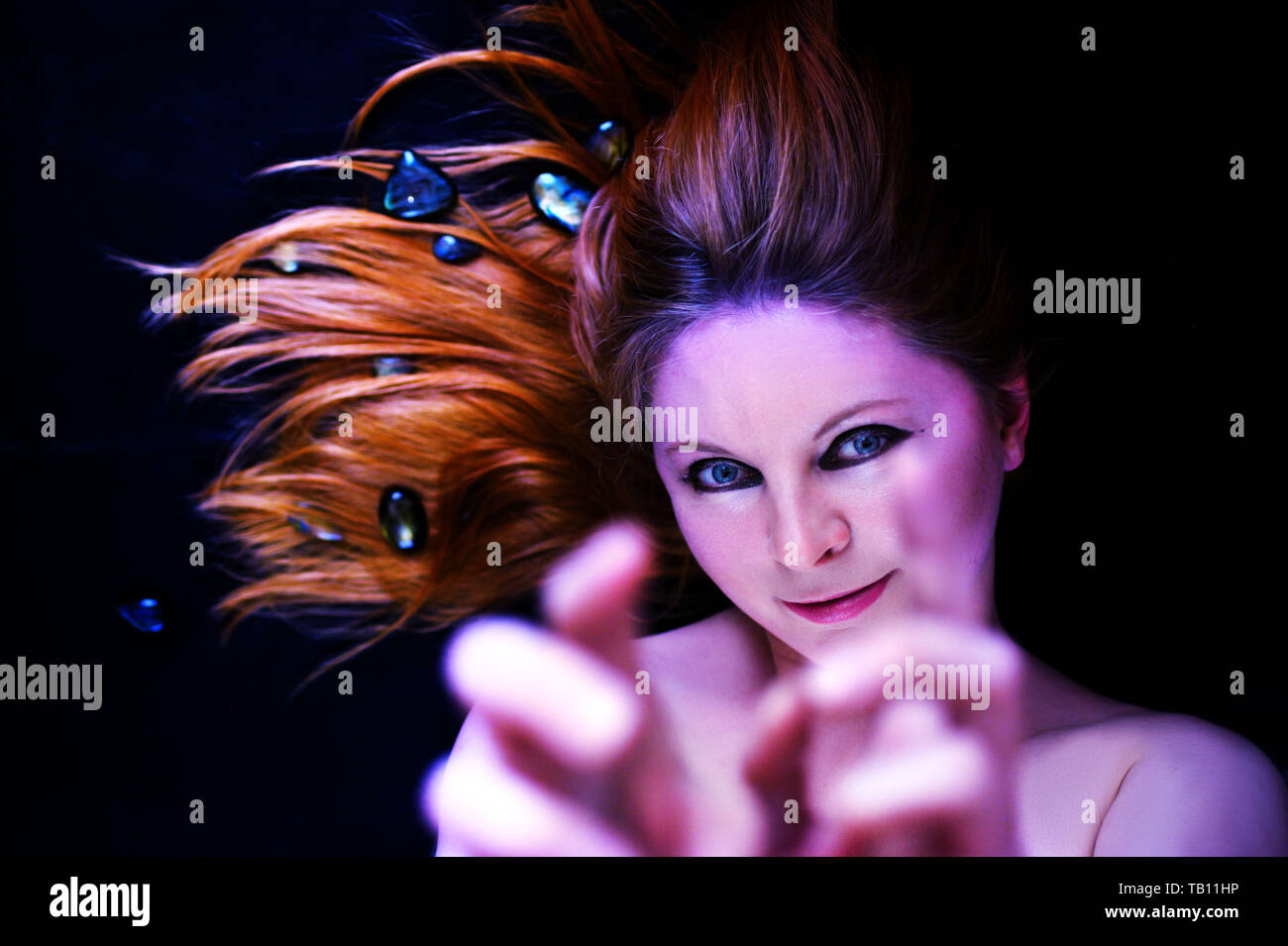 Red hair woman laying on the black floor. She is smiling. Fantasy or dream photo. Stock Photo