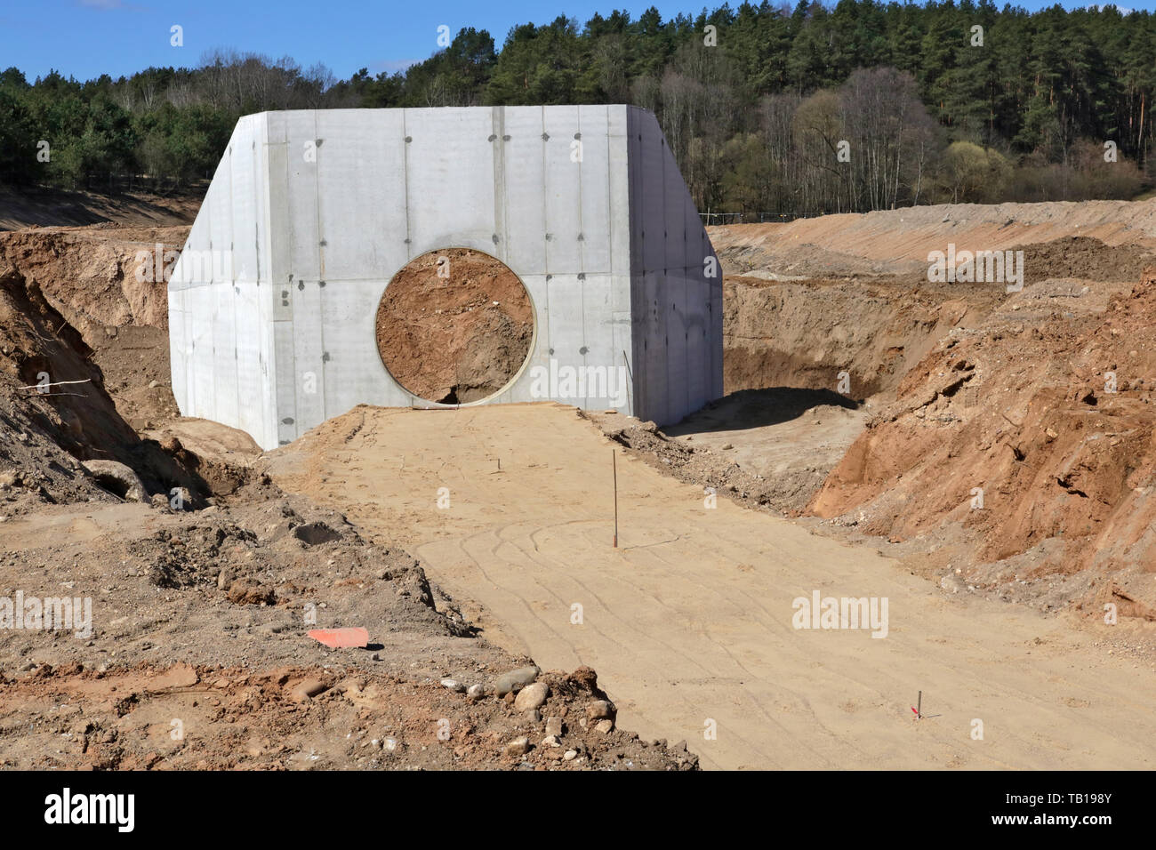 Large  concrete collector for  sewer pipes  and heaps of sand with traces of heavy equipment wheels on a construction site in the forest. Stock Photo