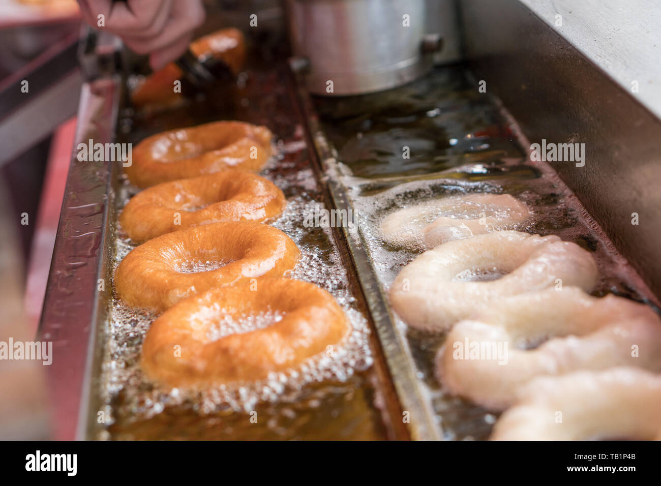 Donut making machine frying donuts in hot oil. Unhealthy junk food