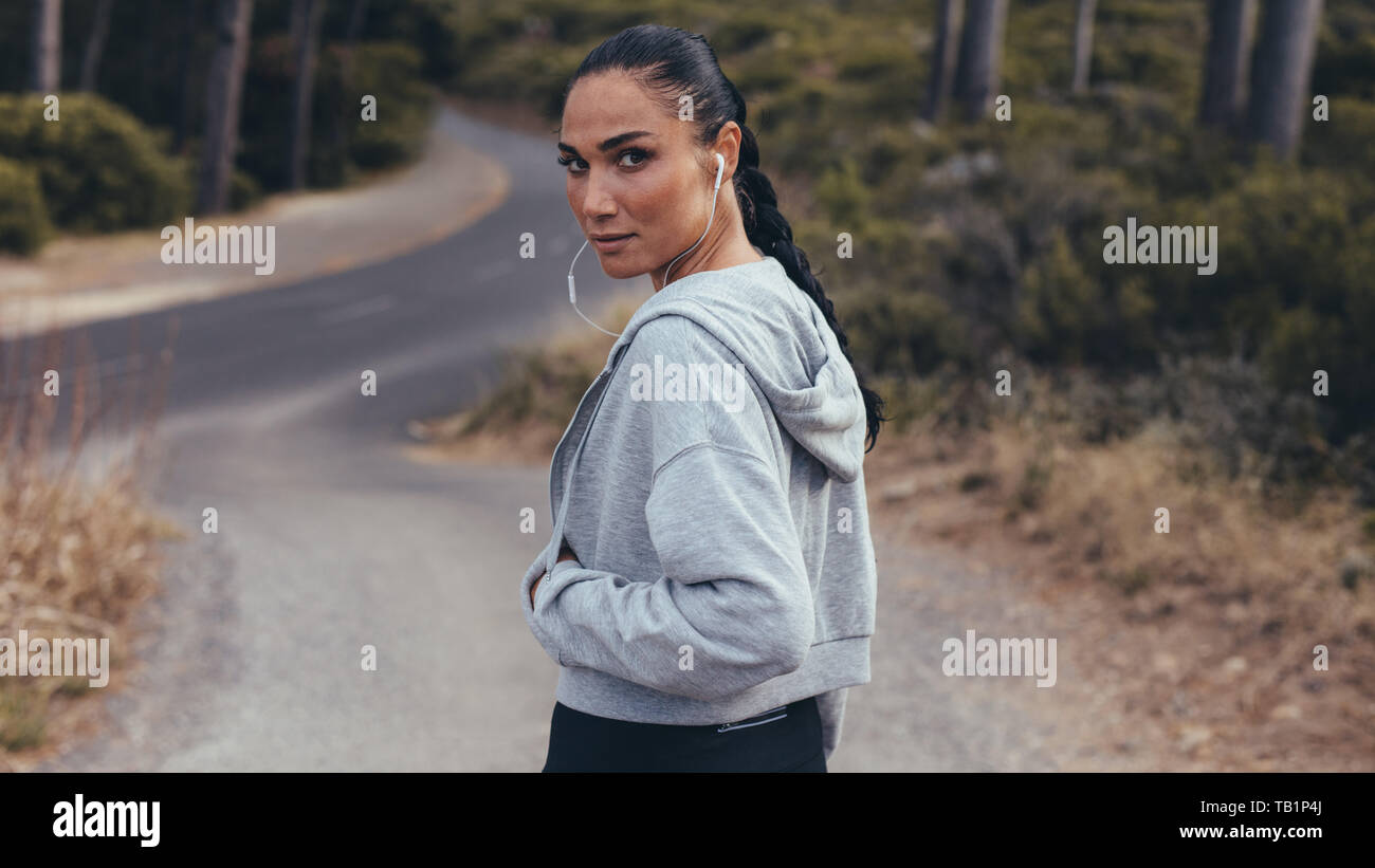 Rear view of fitness woman walking on country road and looking over her shoulder. Sporty woman on cross country path. Stock Photo