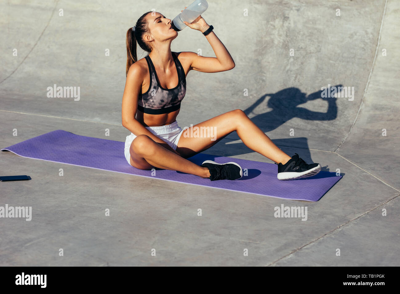 Female sitting on fitness mat and drinking water. Fitness woman drinking water from a after workout Stock Photo Alamy