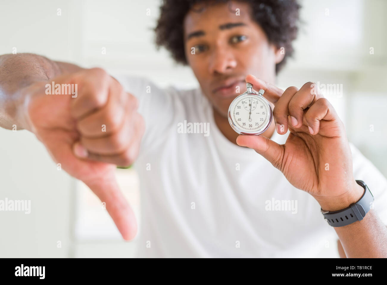 African American man holding stopwatch with angry face, negative sign ...
