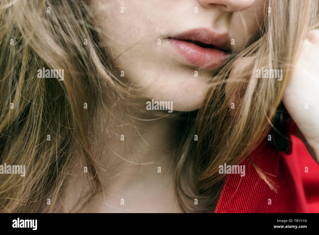 Young blonde woman with beautiful full lips. Resting chin on hand, wearing a fashionable silver ring. Blonde hair in the wind Stock Photo