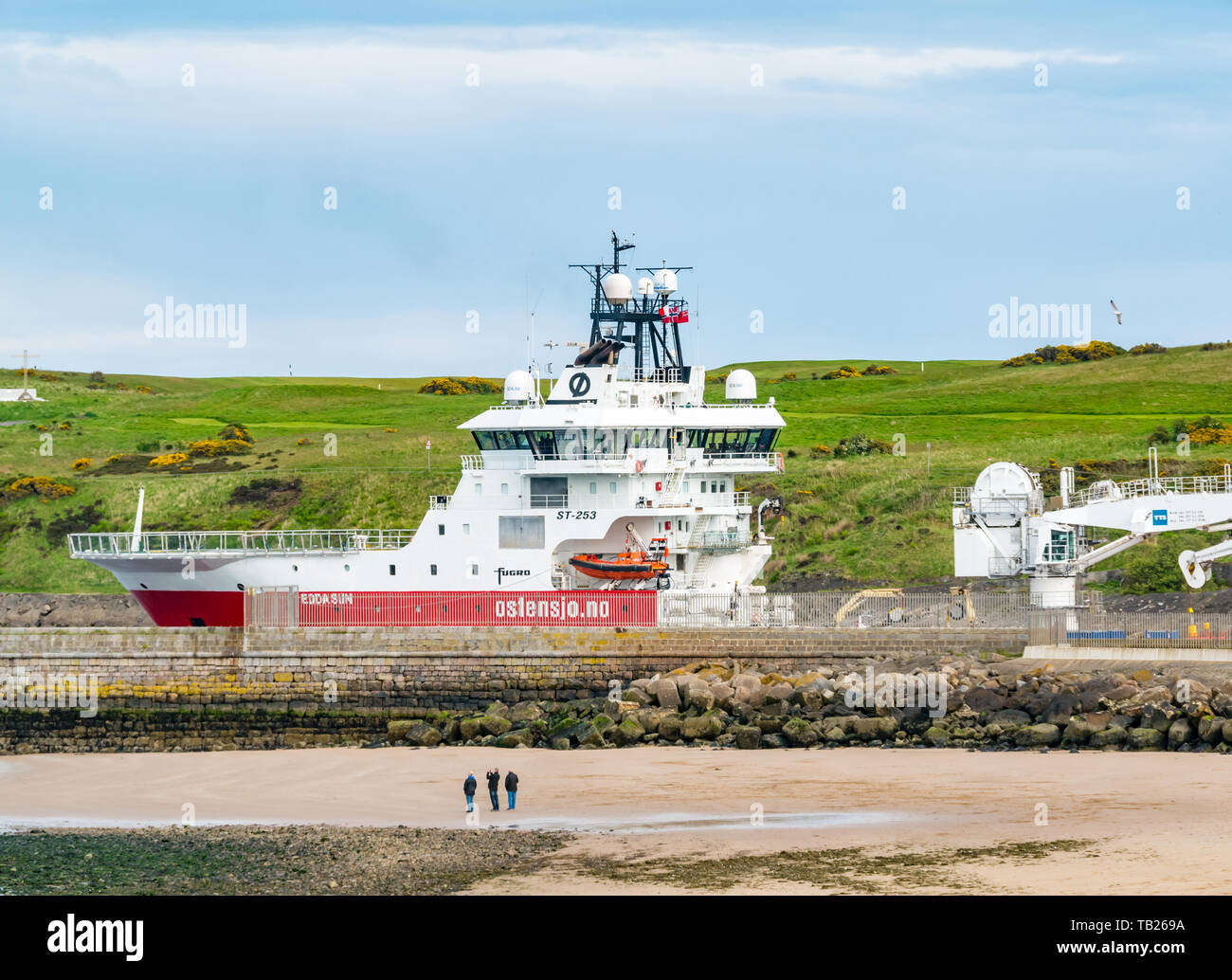 Aberdeen, Scotland, United Kingdom, 29th May 2019.  A Ostensjo Rederi Norwegian research/survey vessel, Edda Sun, leaves the harbour and sets sail for the North Sea as people enjoy an evening walk on the beach near Footdee and the old fisherman cottages Stock Photo