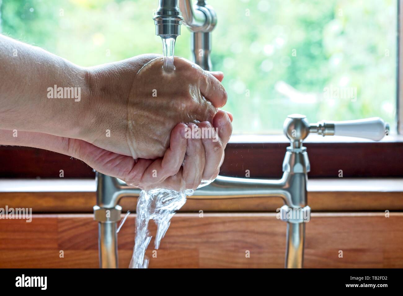 Man washing hands under taps at a kitchen sink in the Uk Stock Photo