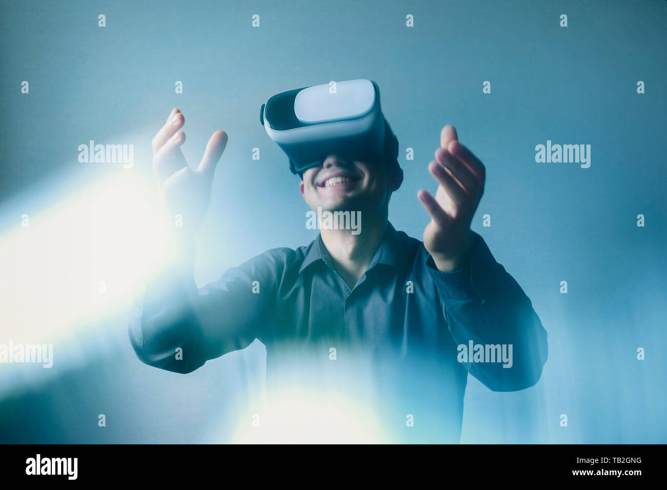 Man wearing virtual reality headset or goggles gesturing with his hands with atmospheric light flare in a conceptual image Stock Photo