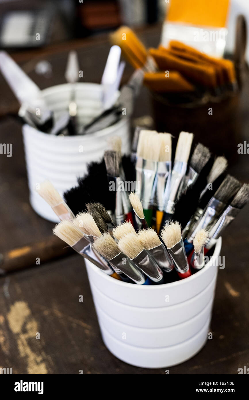 High angle close up of white ceramic pot with selection of paintbrushes in various sizes. Stock Photo