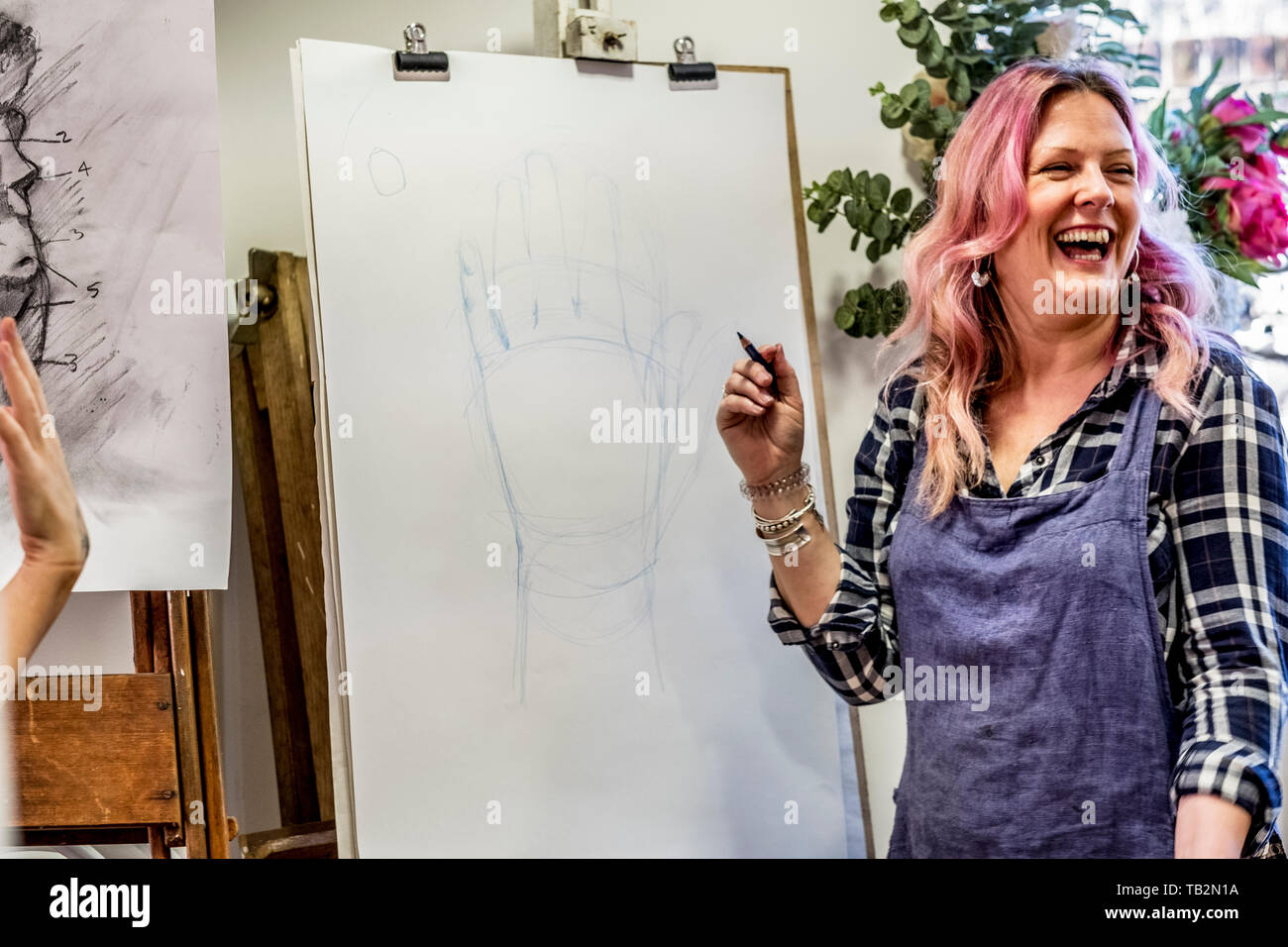 Laughing woman wearing apron standing at an easel, drawing of human hand. Stock Photo