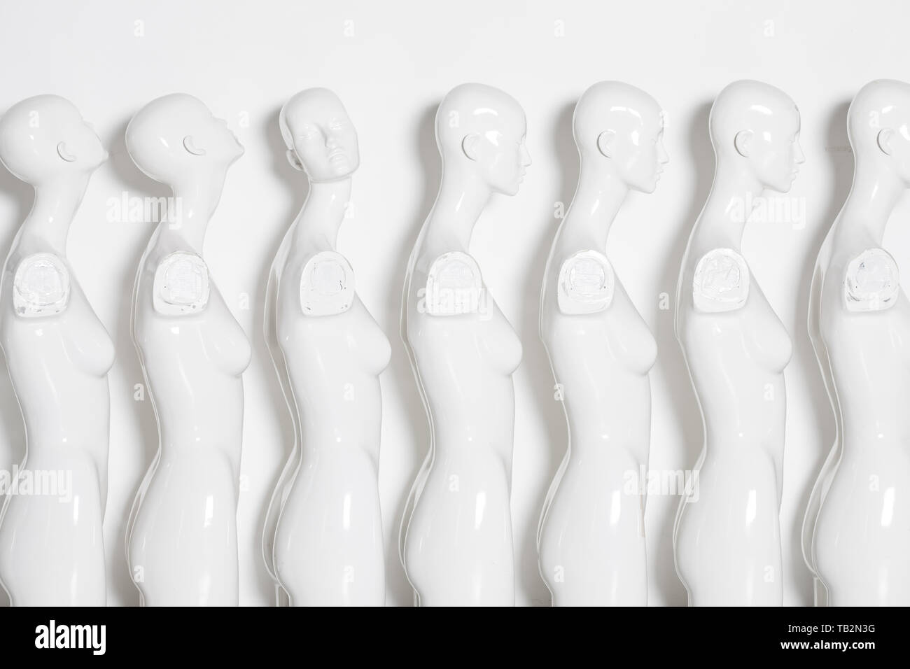 High Key Bright Picture of White Woman Torso Figurines Standing in The Line All But One Looking to Same Direction. Stock Photo