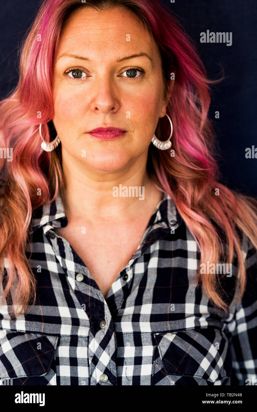Portrait of woman with long blond wavy hair with pink streaks wearing black and white checkered shirt and hoop earrings. Stock Photo