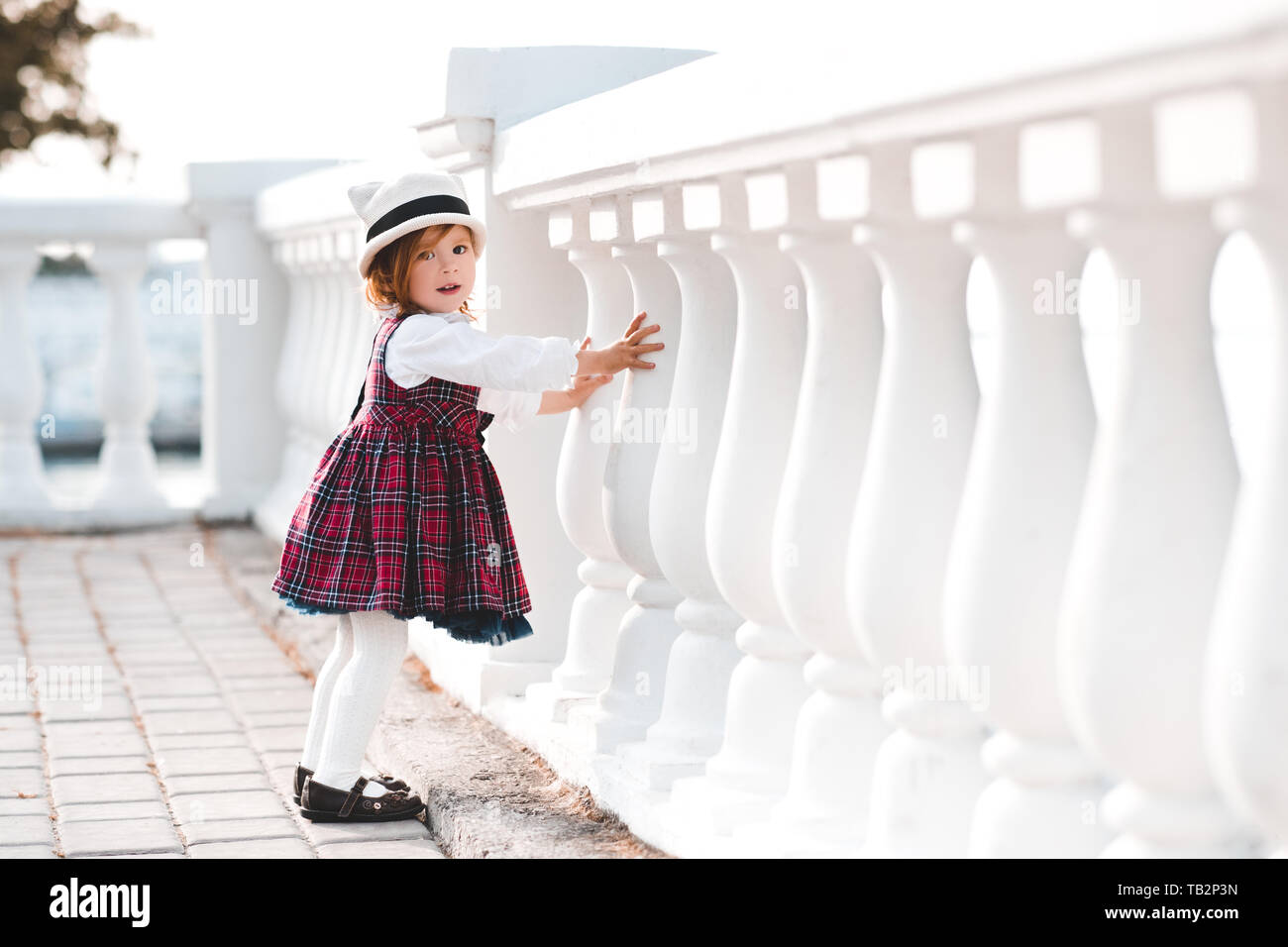 Funny pre school baby girl 2-3 year old wearing stylish dress and hat outdoors. Looking at camera. Stock Photo