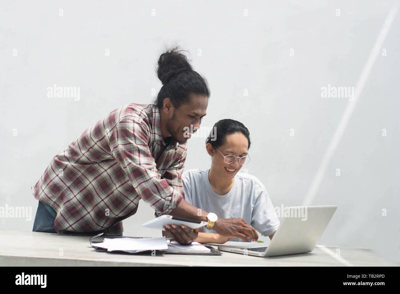 two friend with diffrent ethnic working together with laptop and tablet discussing something, two young man working and studying together Stock Photo