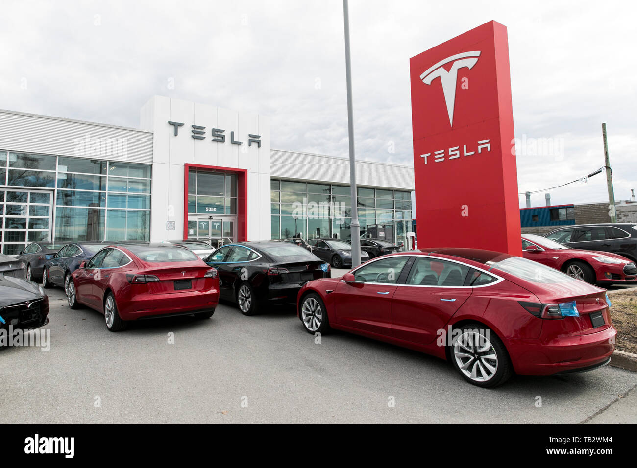 A logo sign outside of a Tesla car dealership with Model 3 and Model S cars in the lot in Montreal, Quebec, Canada, on April 21, 2019. Stock Photo