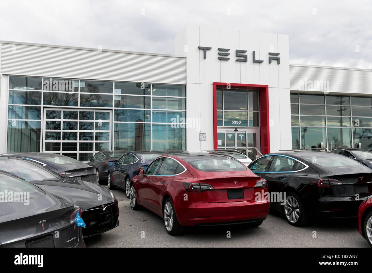 A Logo Sign Outside Of A Tesla Car Dealership With Model 3