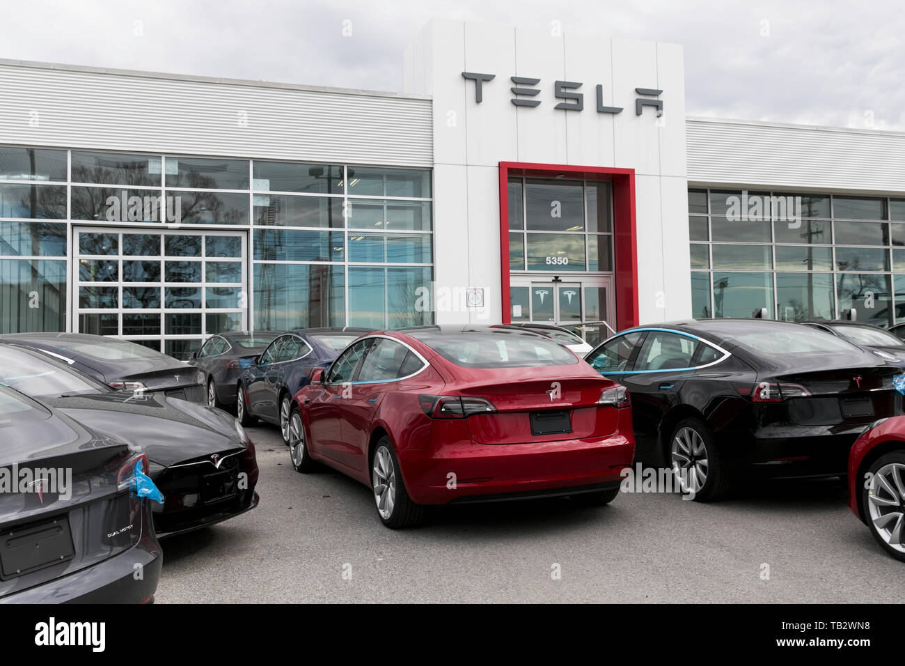 A logo sign outside of a Tesla car dealership with Model 3 and Model S cars in the lot in Montreal, Quebec, Canada, on April 21, 2019. Stock Photo