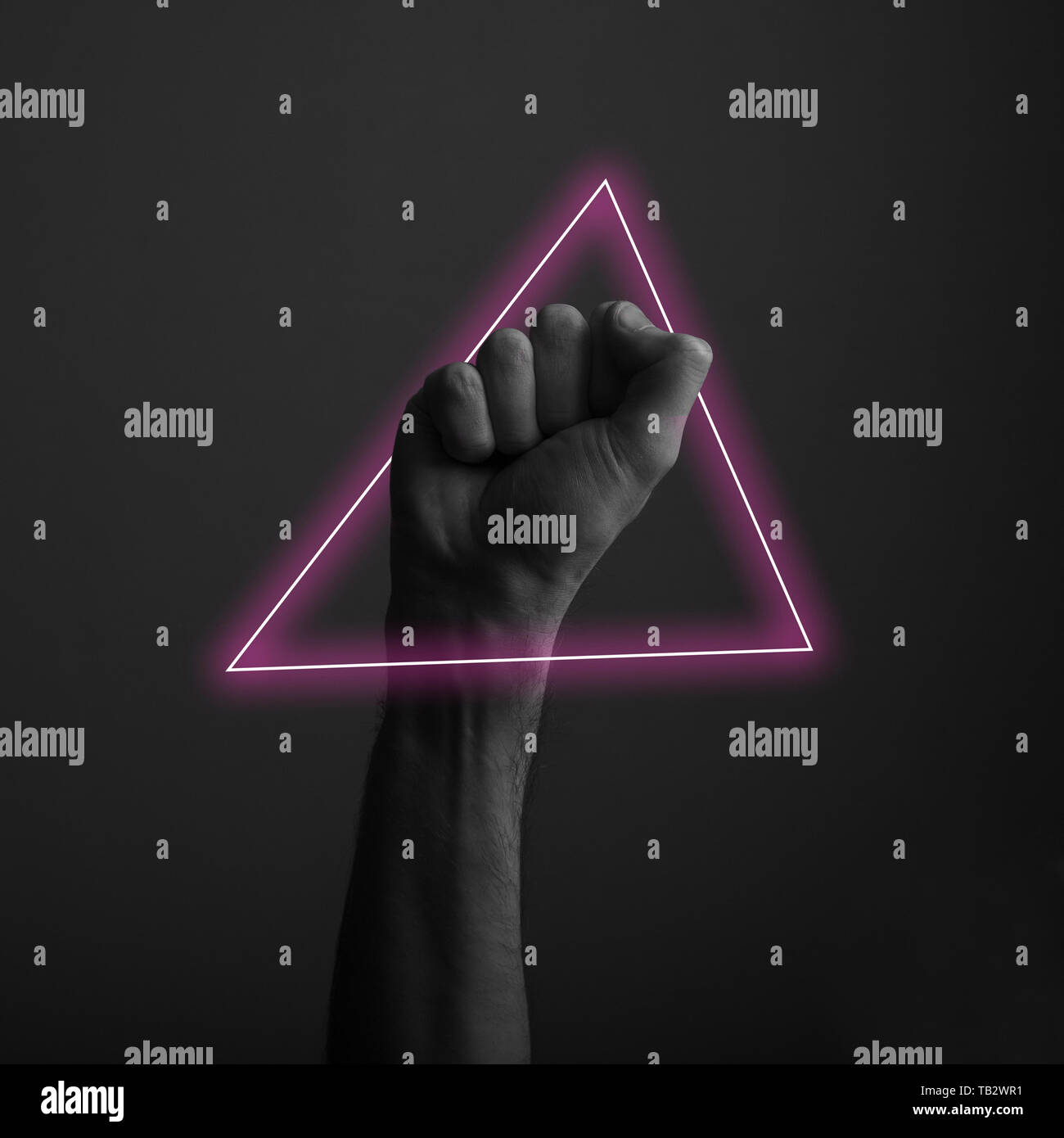 Raised clenched fist against a dark background with abstract neon light glow Stock Photo