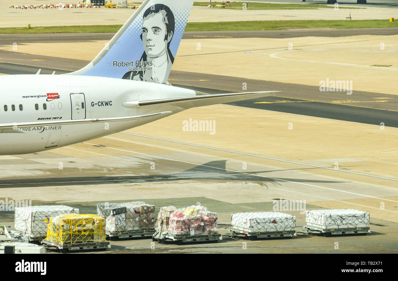 LONDON GATWICK AIRPORT, ENGLAND - APRIL 2019: Air freight on trucks in from of a Norwegian Air plane at London Gatwick Airport. . Stock Photo
