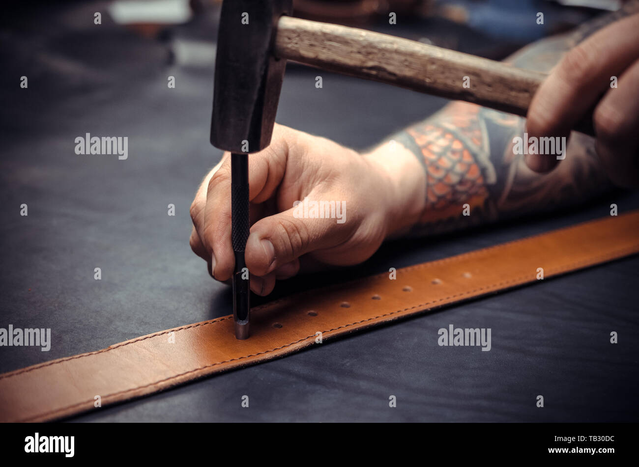 Handicraftsman processing a leather workpiece at the workshelf Stock Photo