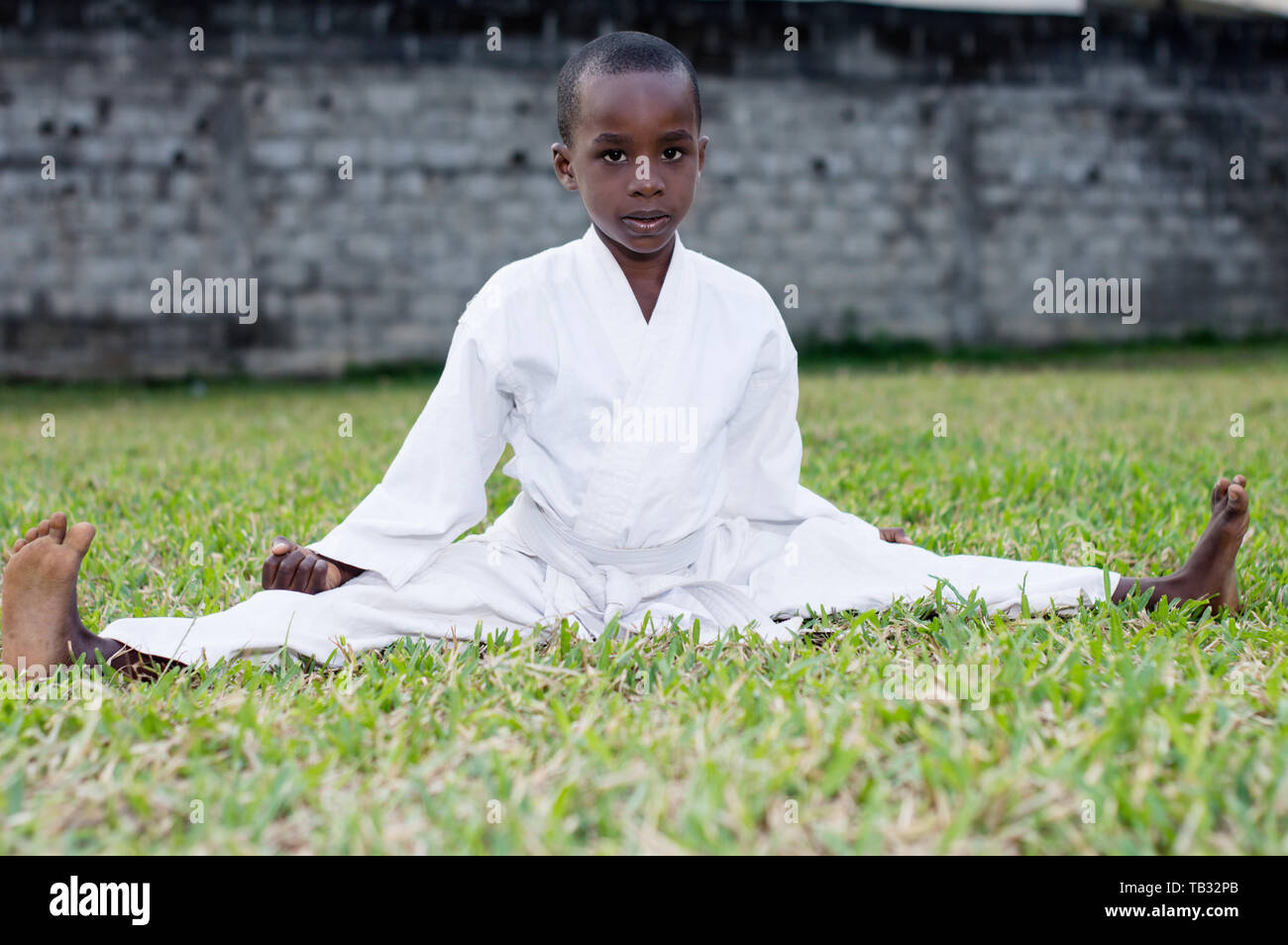 Little boy fighting in karate outfit sitting and showing martial art gesture in the park Stock