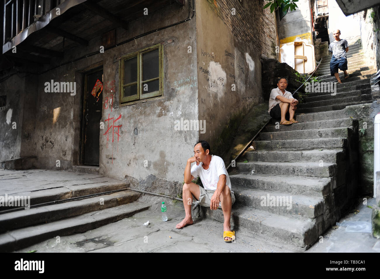 04.08.2012, Chongqing, , China - Men are sitting on the steps in front of a house in the Altsatdt of Chongqing, on the wall of which red letters infor Stock Photo