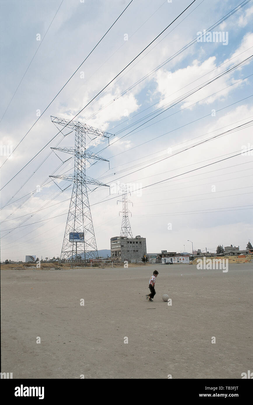 A boy plays football alone under enormouse electricity towers. Toluca, Mexico, March 20, 2006. Football llanero, which translates  as street football  Stock Photo