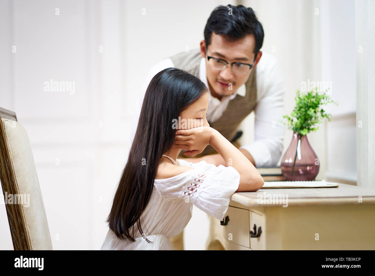 sad little asian girl sitting at desk in her room and getting comfort from caring father Stock Photo