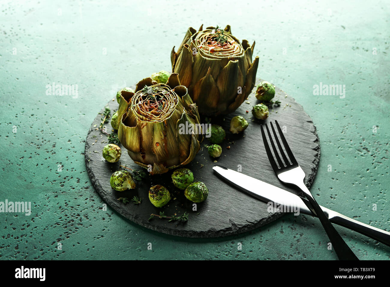 Slate plate with tasty baked artichokes and Brussels sprouts on table