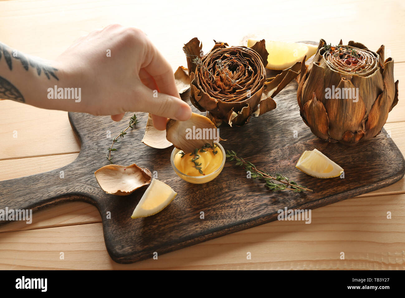 Woman eating tasty baked artichoke with sauce, closeup Stock Photo