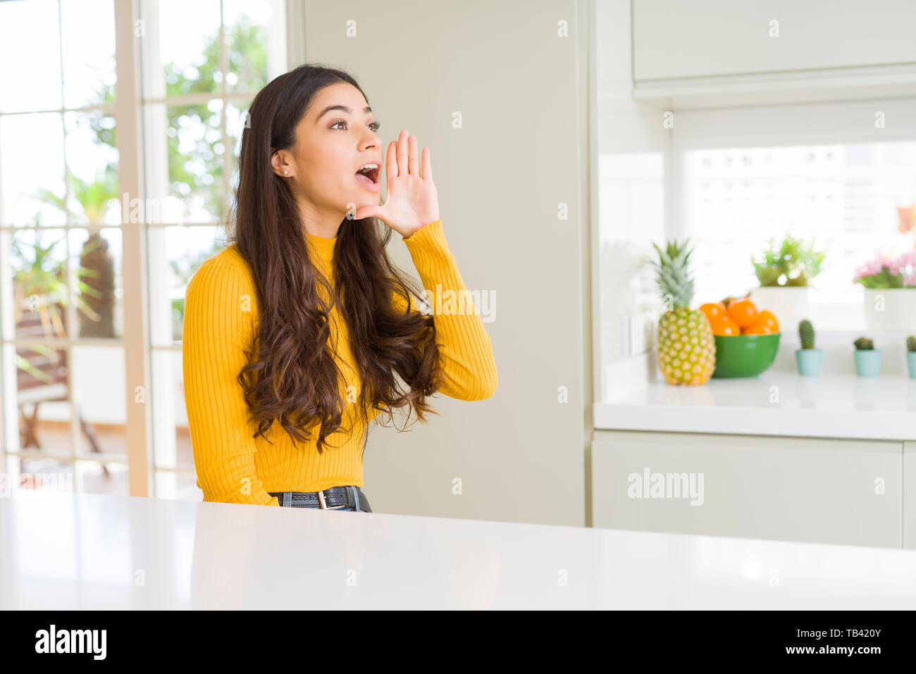 Young beautiful woman at home on white table shouting and screaming ...