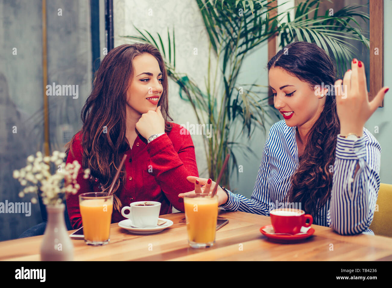 Two beautiful young women sitting in a cafe, drinking coffee and having