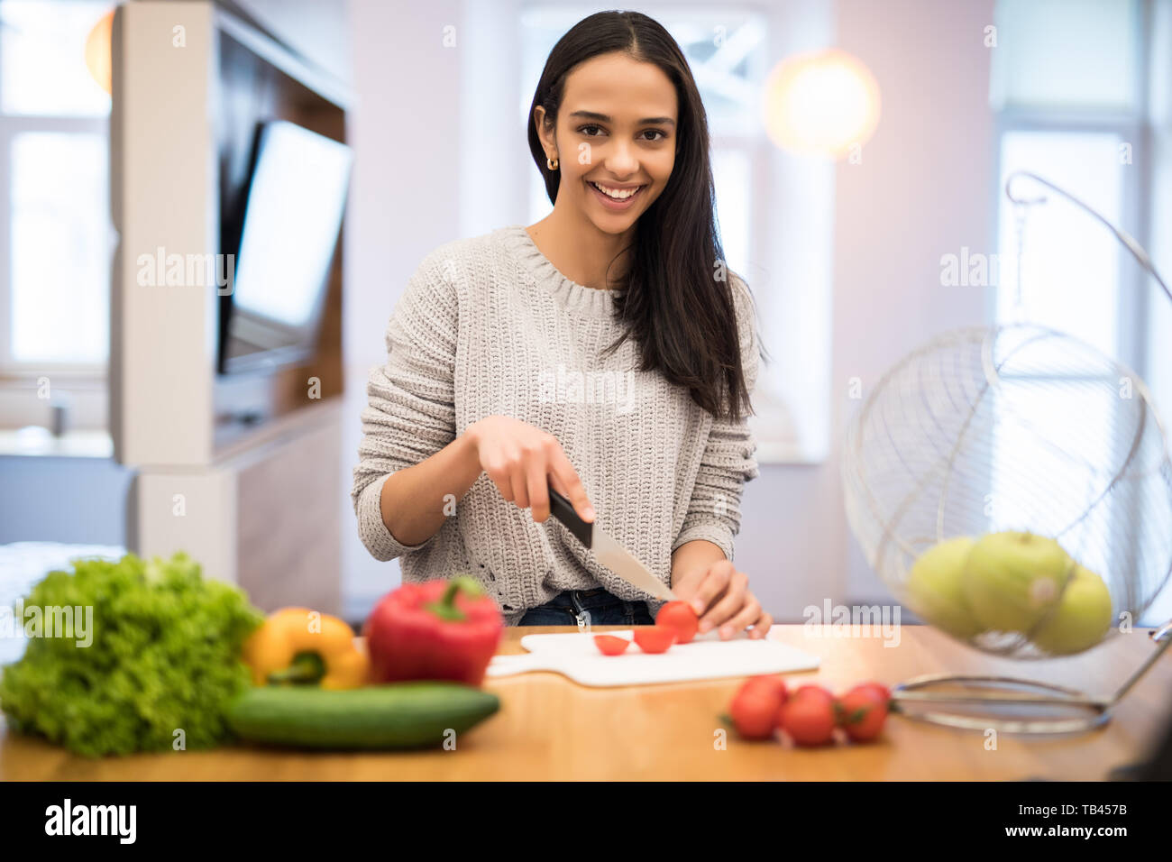 The young woman cuts vegetables in the kitchen with a knife and laptop on the table. Vegetable Salad. Diet. Dieting Concept. Healthy Lifestyle. Cookin Stock Photo