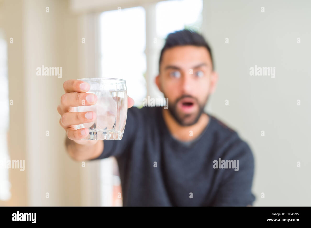 Handsome hispanic man drinking a fresh glass of water scared in shock