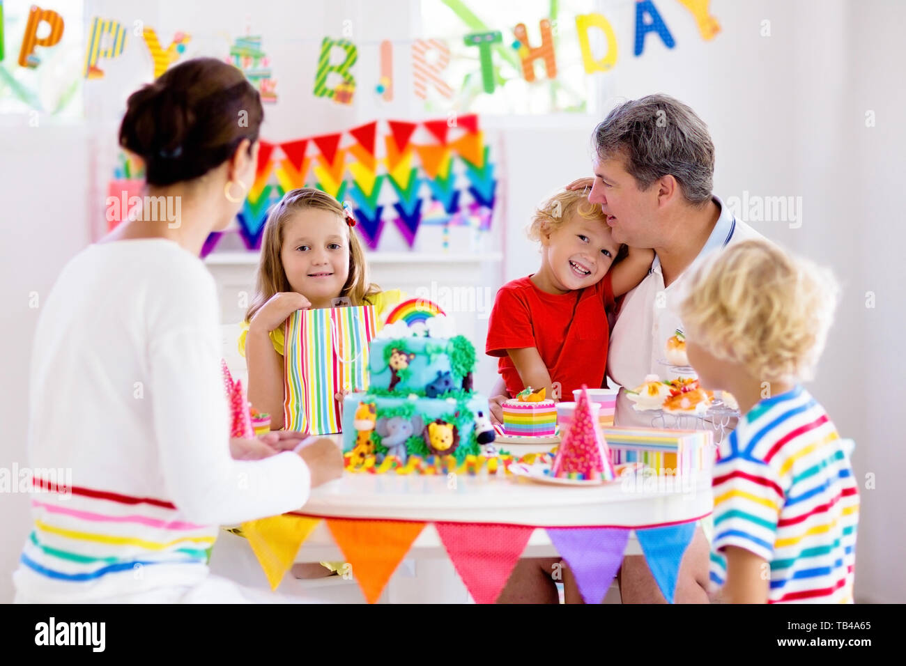Kids birthday party. Child blowing candles on cake and opening presents