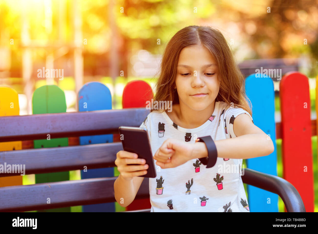 Smiling little girl using modern wearable smart watch and mobile phone outdoor synchronizing apps Stock Photo