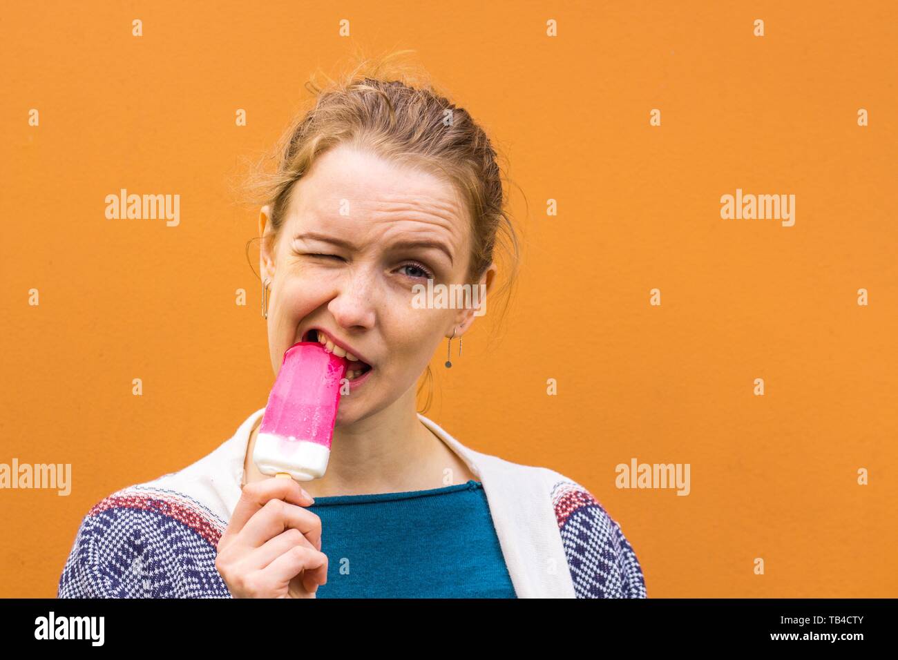 Beautiful and young girl eats a pink hue ice cream and enjoys. She closed her eyes from the cold of the ice cream but continues to enjoy. Stock Photo