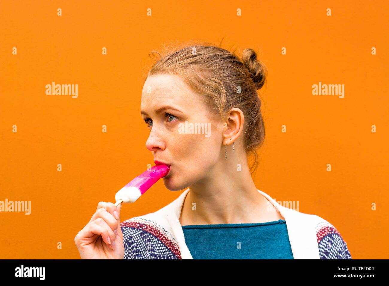 Beautiful and young girl eats a pink hue ice cream and enjoys. She stands against a pink shade. Stock Photo