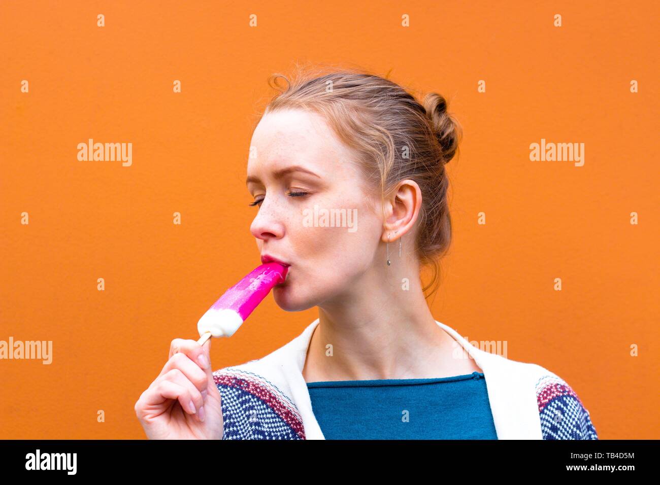 Beautiful and young girl eats a pink hue ice cream and enjoys. She closed her eyes from enjoying the ice frost Stock Photo
