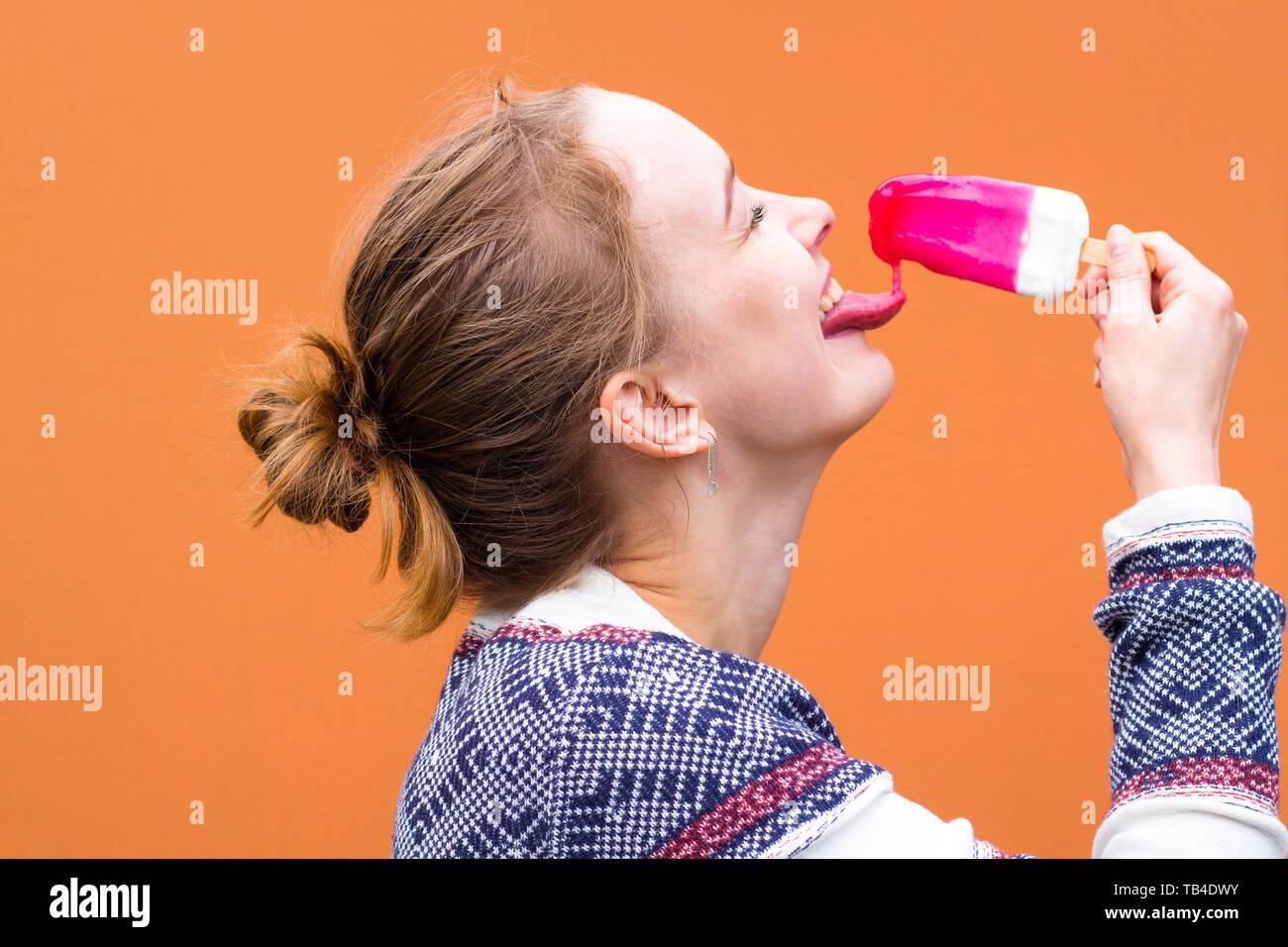 Beautiful and young girl eats a pink hue ice cream and enjoys. She catches a drop of melted ice cream with her tongue and smiles. Stock Photo