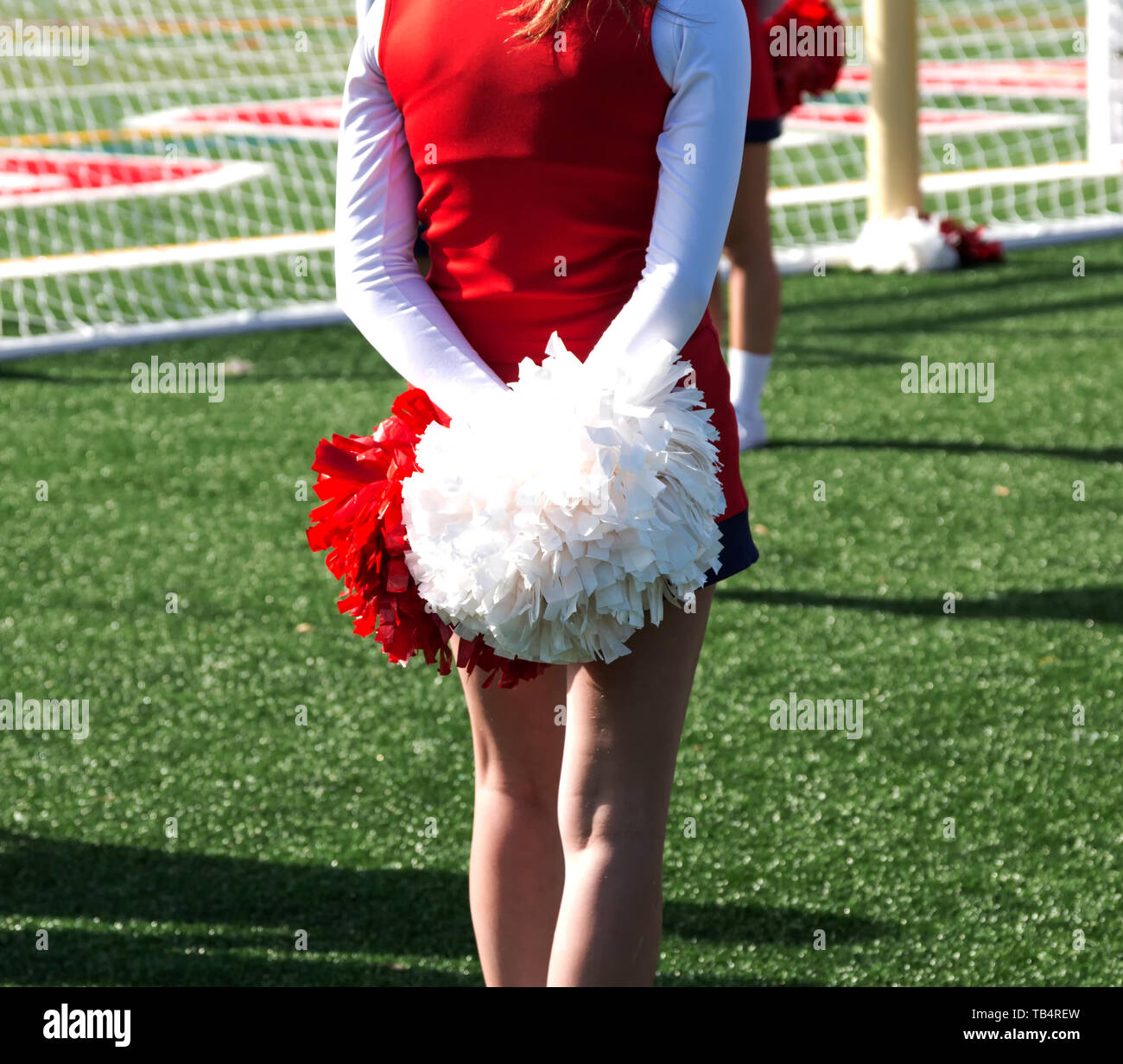 A high school cheerleader is standing tall with her red and white pompoms behind her. Stock Photo