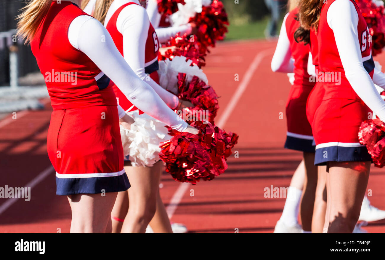High school cheerleaders have their pompoms in front of them while watching the football game waiting to cheer. Stock Photo