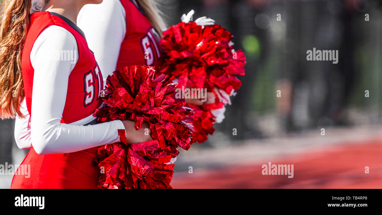 Two high school cheerleaders with red and white pom poms at a football game in autumn. Stock Photo