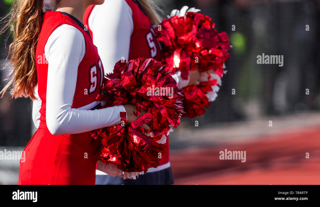 Two high school cheerleaders with red and white pompoms are watching the football game ready to cheer for their team. Stock Photo