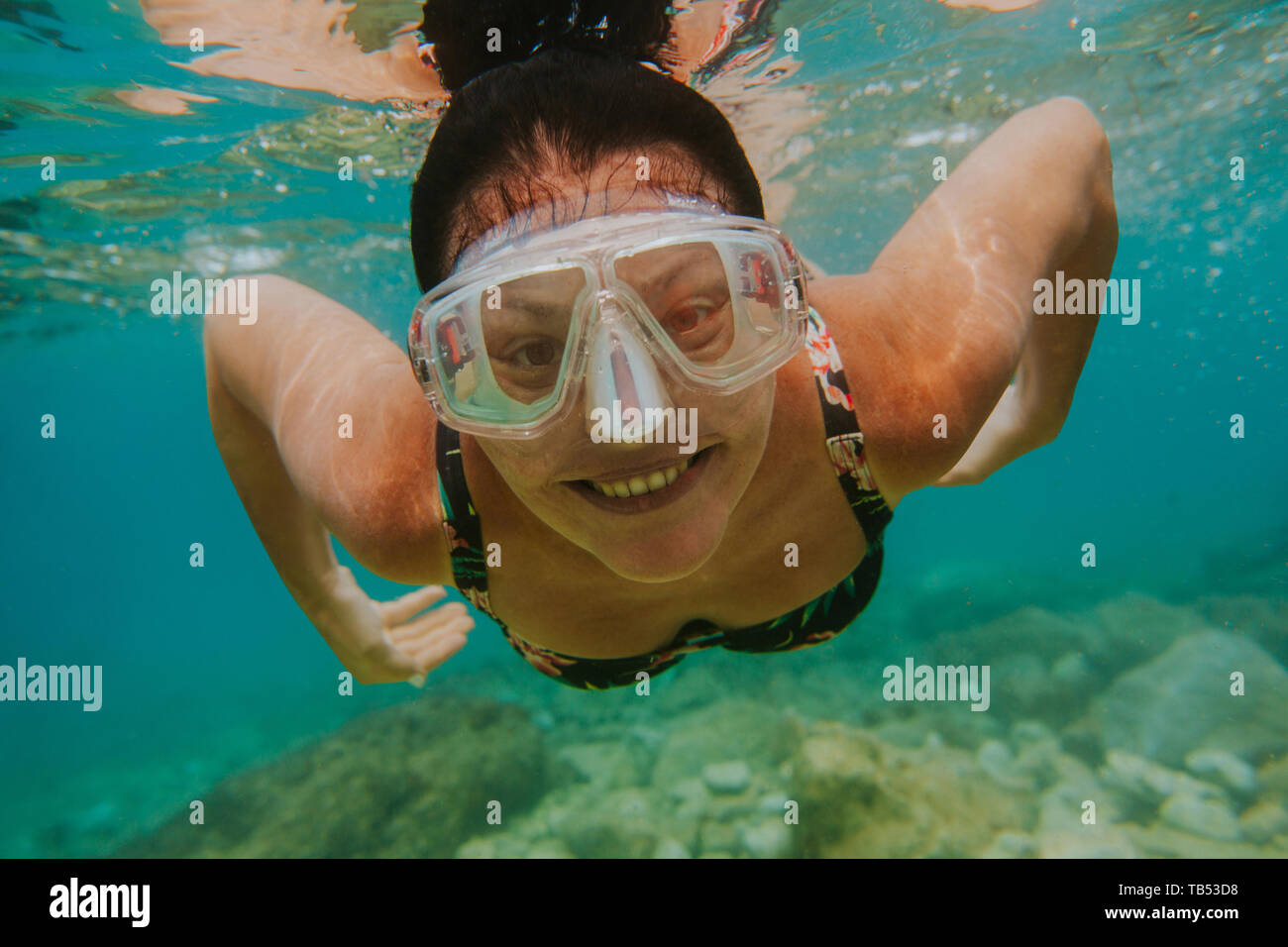 Cheerful woman swimming under sea. Smiling female swimmer with diving mask looking into camera underwater. Stock Photo