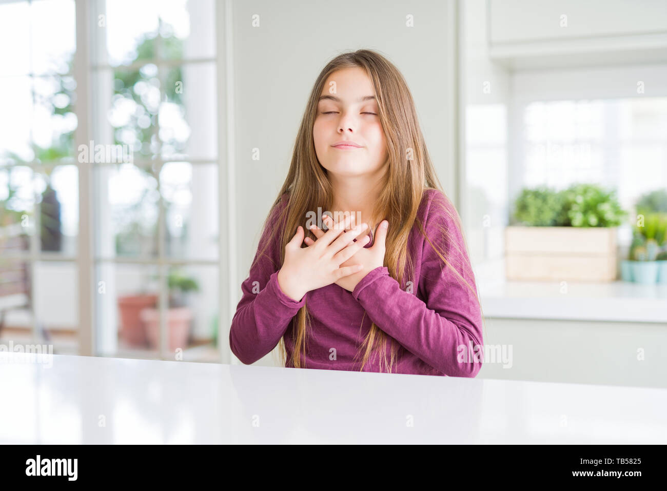 Beautiful young girl kid on white table smiling with hands on chest ...