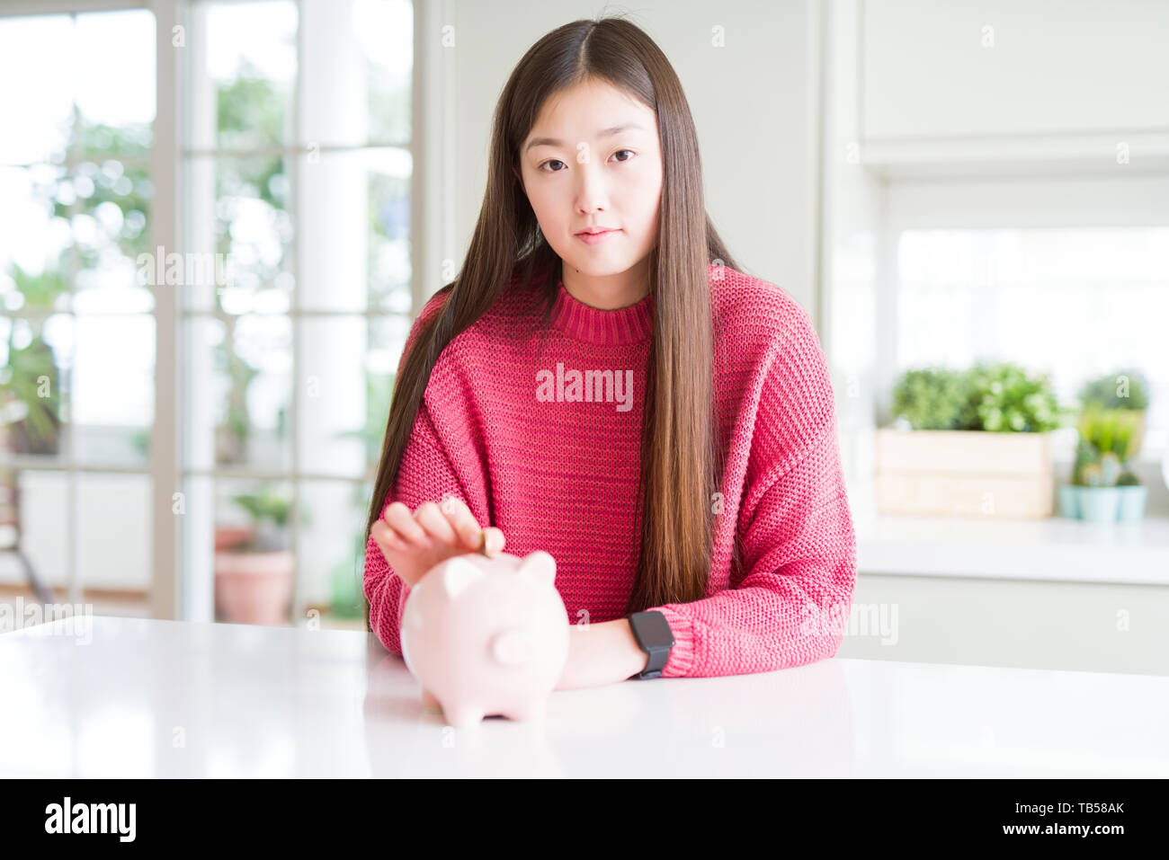 Beautiful Asian woman putting a coin inside piggy bag with a confident ...