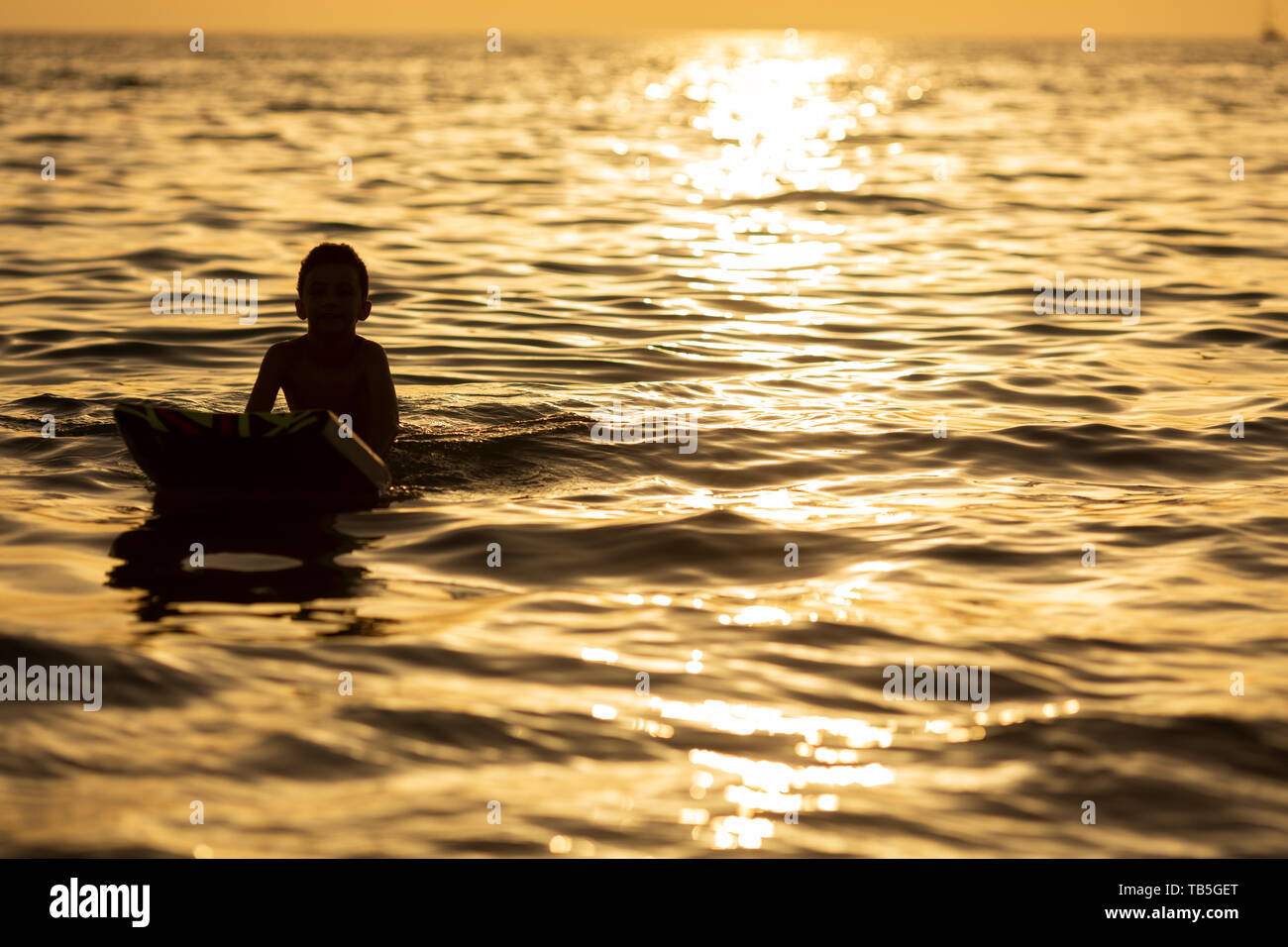 alone boy silhouette on a board in the sea at sunset Stock Photo ...